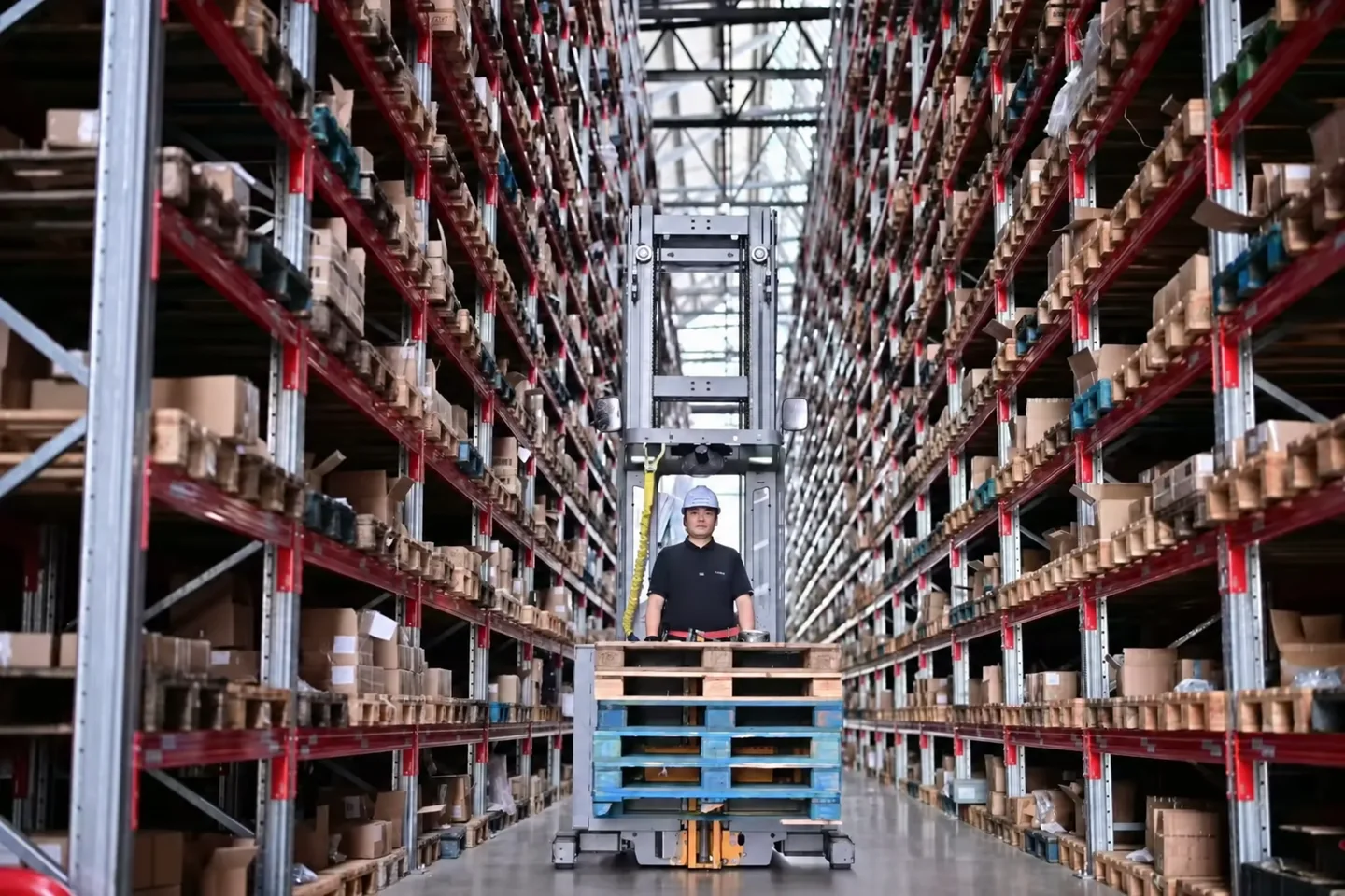 Forklift operator in a long aisle between red warehouse racks