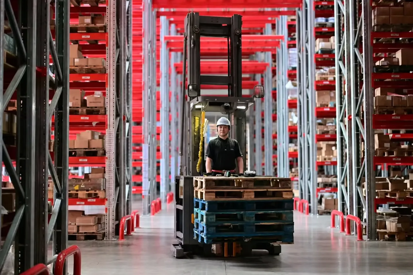 Forklift working between tall red warehouse pallet racks
