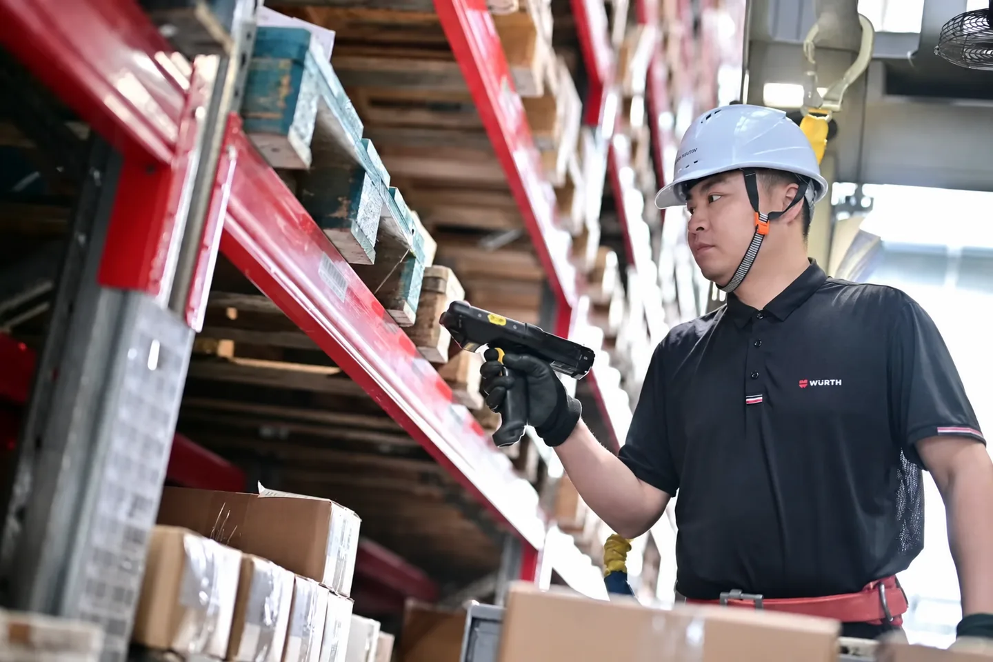 Warehouse operator checking stock beside red pallet racks