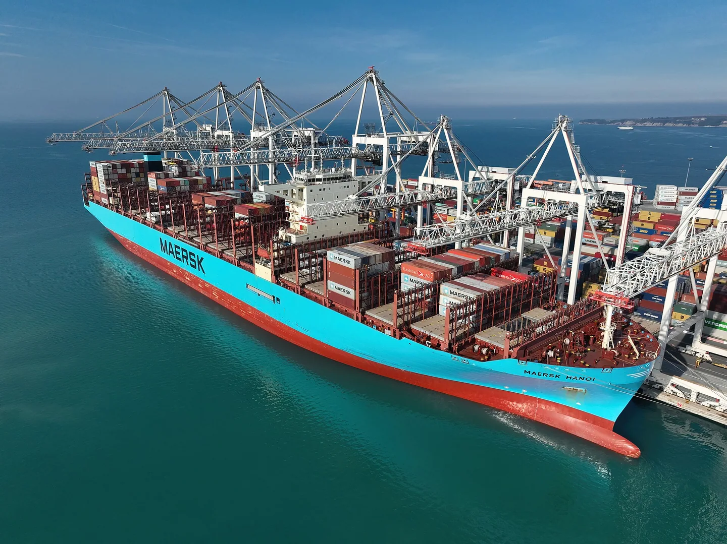 Turquoise container ship alongside cranes above clear blue-green water