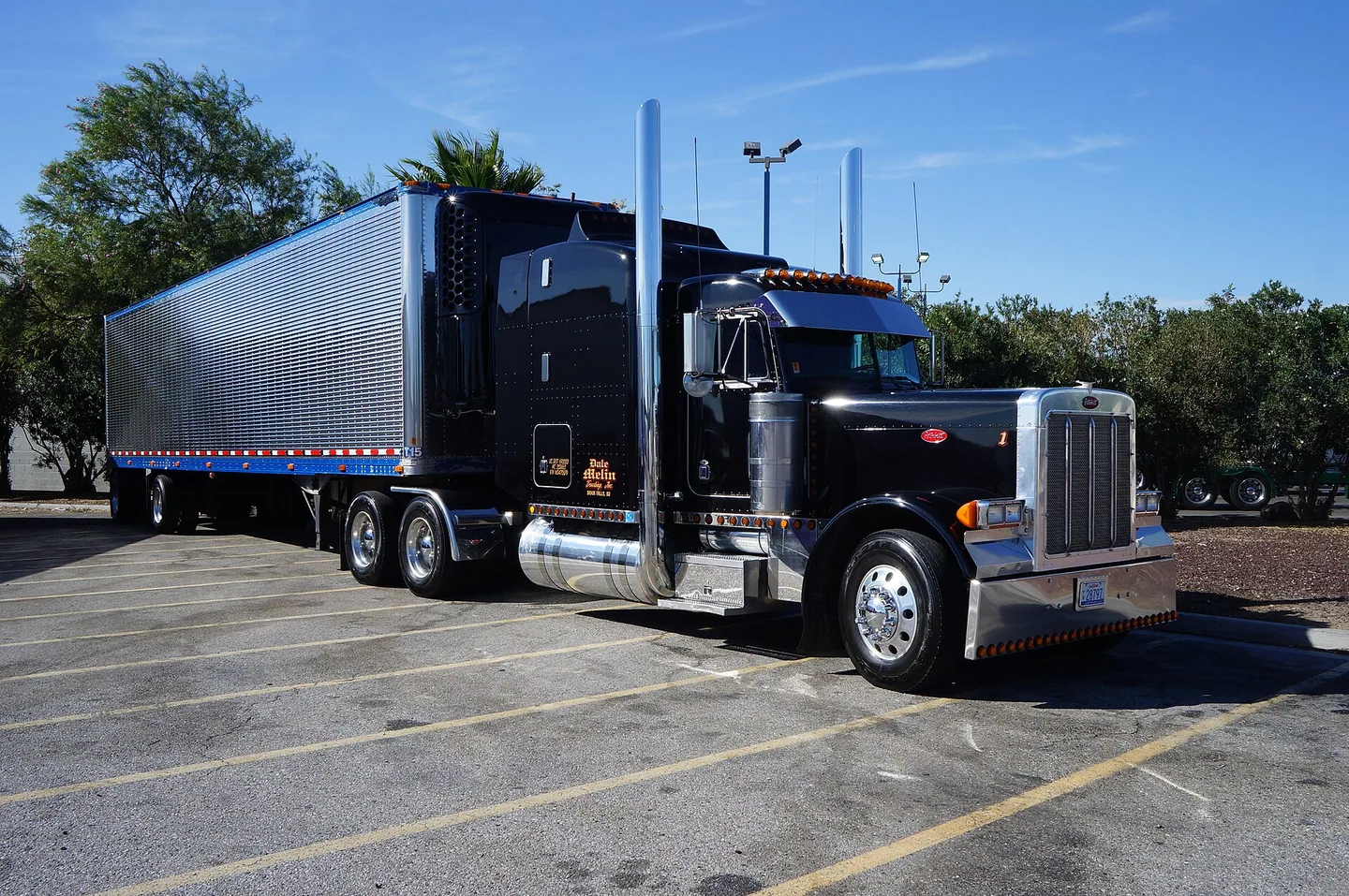 Black articulated truck and silver trailer parked under a blue sky