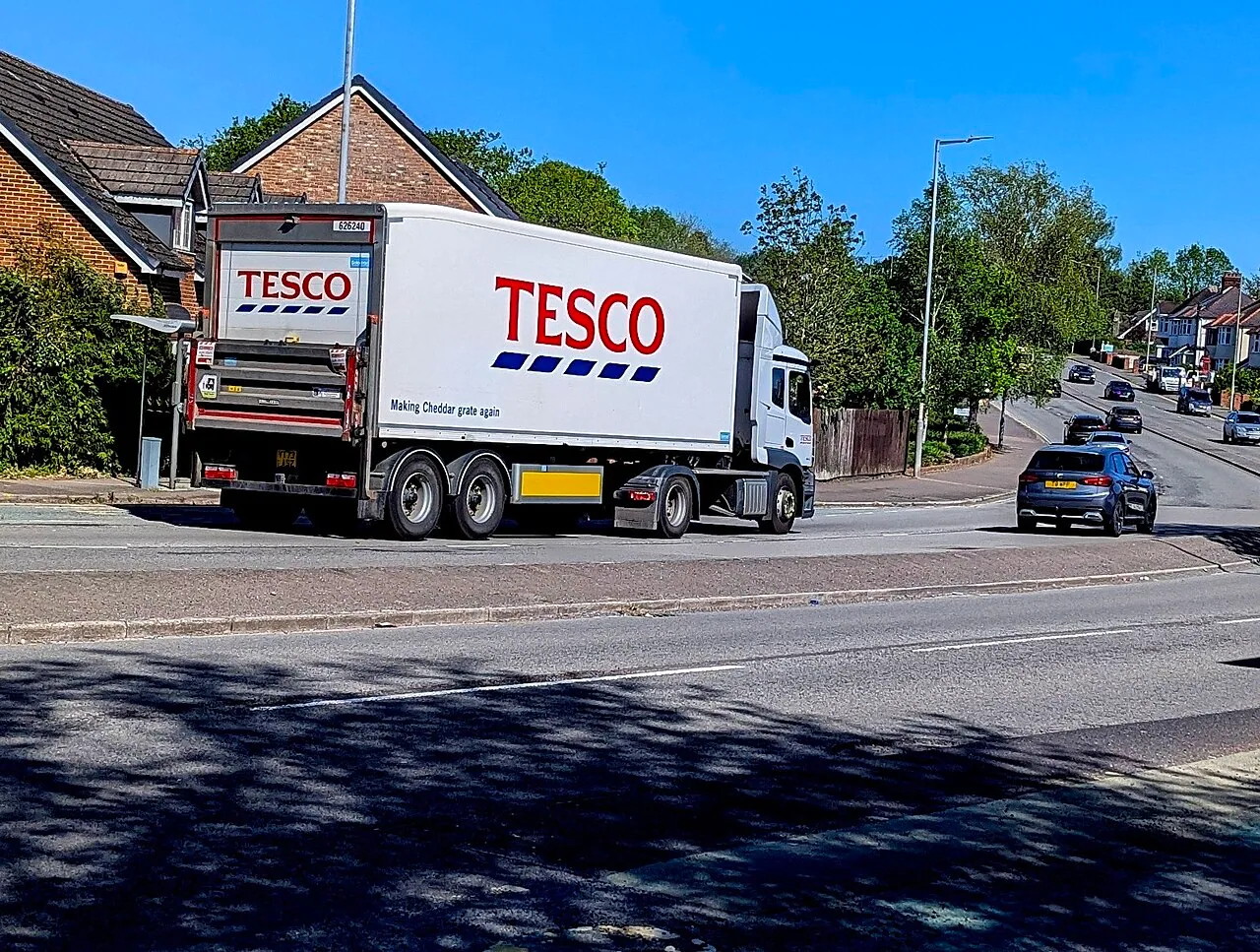 Articulated delivery lorry passing along a tree-lined British road