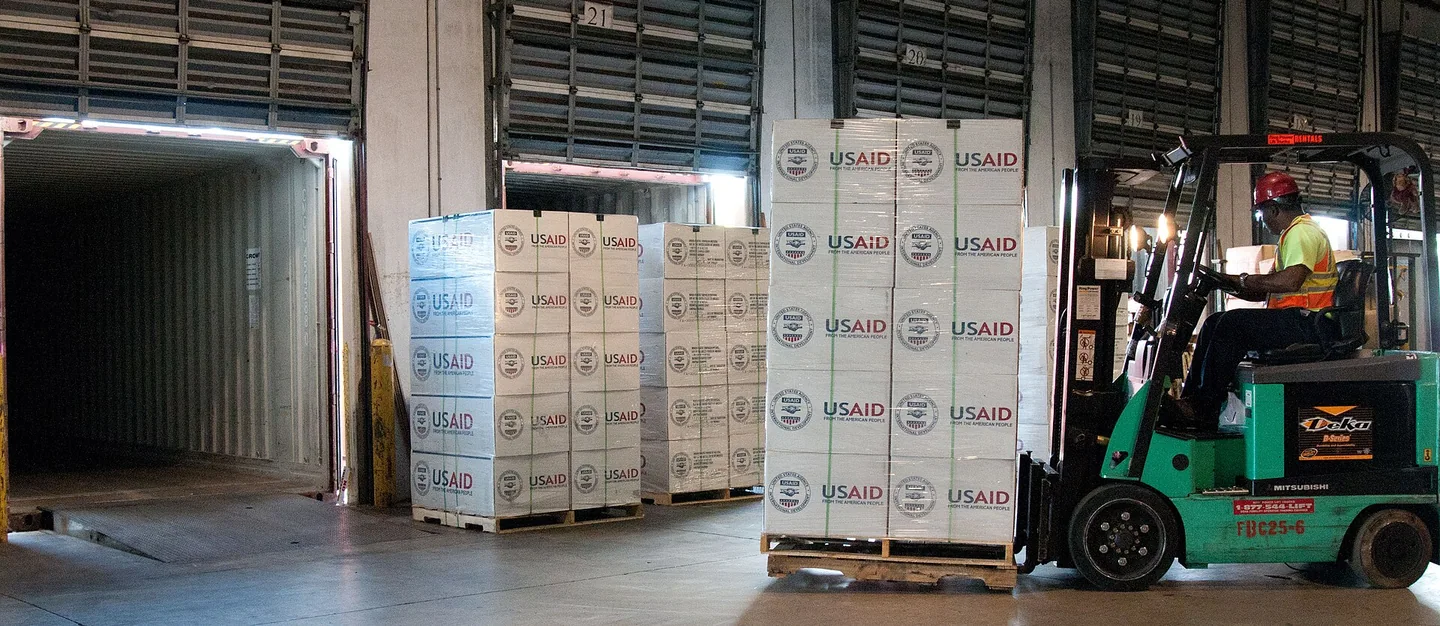 Forklift handling palletised relief supplies beside an open container
