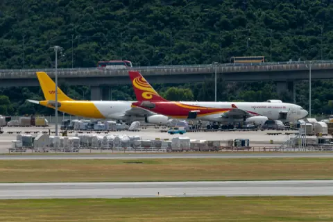 Yellow and red cargo aircraft on a taxiway beneath a green hillside
