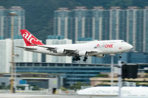 White and red cargo aircraft at an airport beneath a green hillside