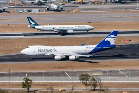 White and blue Network cargo aircraft taxiing past parked airliners