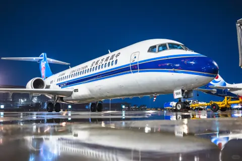 Blue and white passenger aircraft above ground equipment on a wet night apron