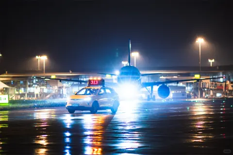 Head-on aircraft lights reflected on a rain-soaked airport apron