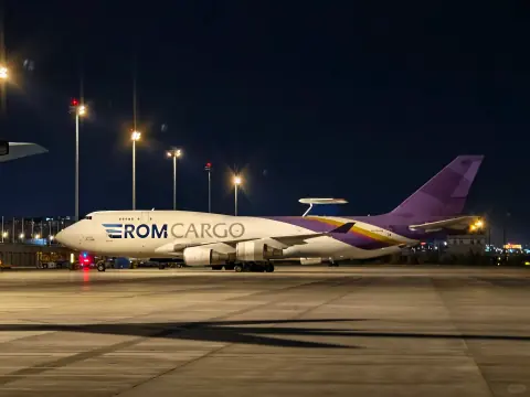 Purple and white cargo aircraft under airport floodlights at night