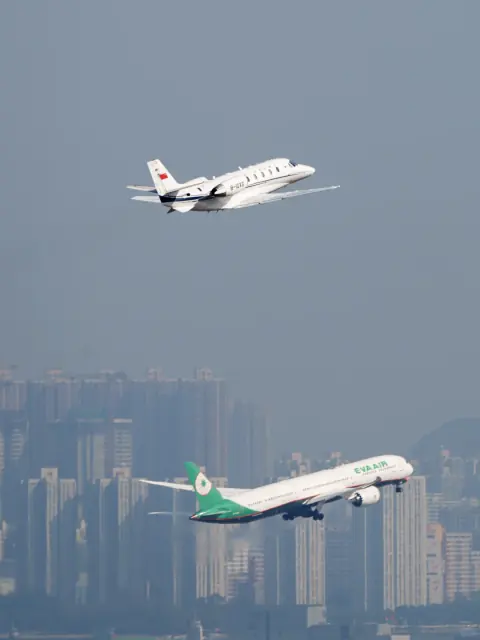 Two aircraft climbing above a distant city skyline