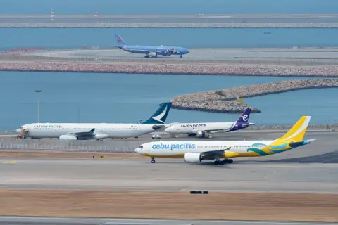 Several aircraft aligned across airport taxiways beside blue water