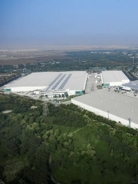 Aerial view of white warehouse roofs beside a belt of trees