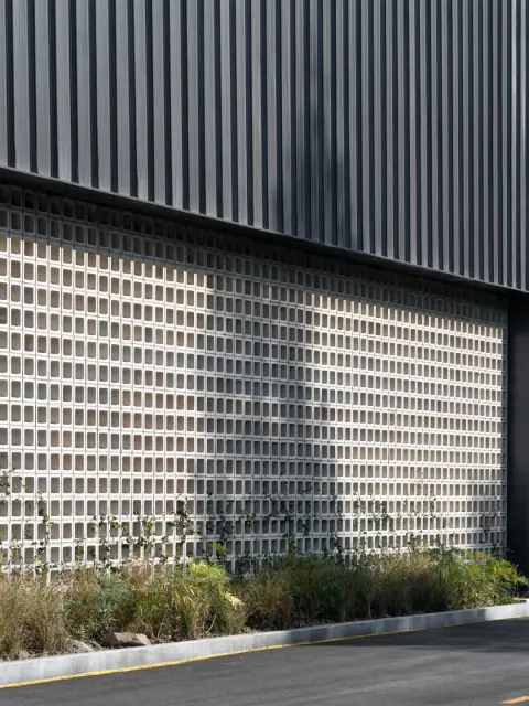 Dark ribbed warehouse cladding above a patterned screen wall
