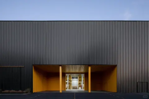 Recessed yellow entrance within a dark metal logistics centre facade