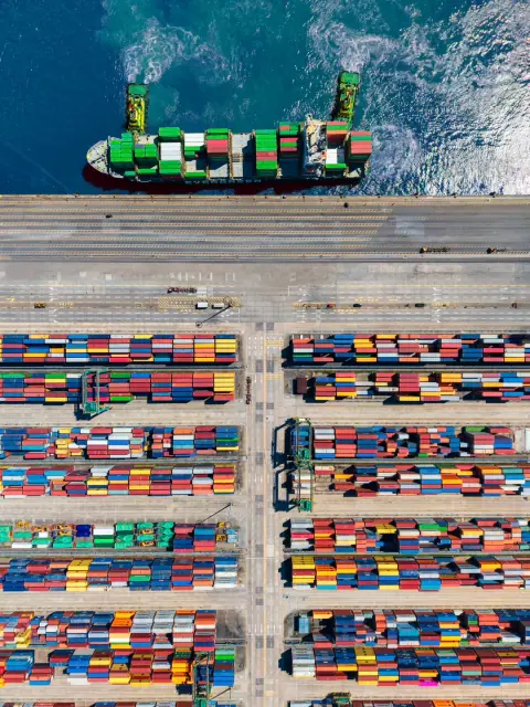 Top-down view of a container ship beside colourful terminal stacks