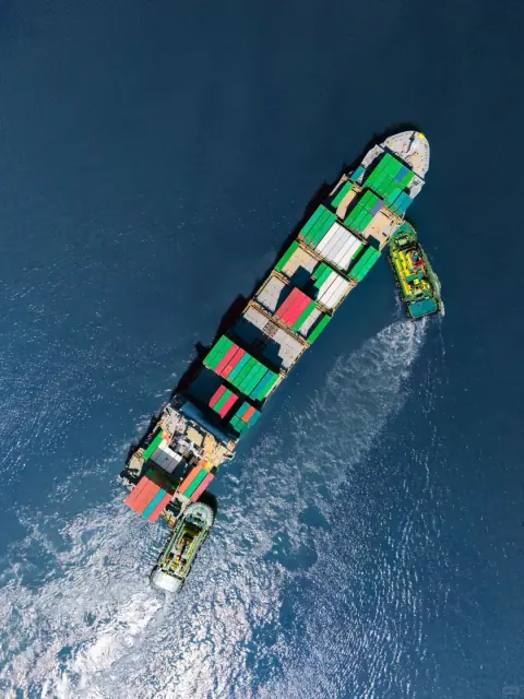 Green-hulled container ship leaving a curved wake in blue water