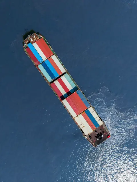 Container ship carrying rows of coloured containers across blue water