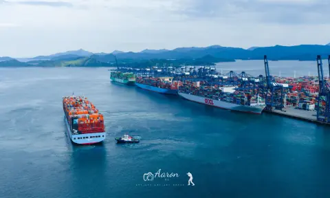 Container ship approaching a busy port with cranes along the quay