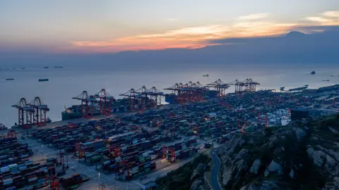 Container terminal and anchored ships beneath a warm sunset sky