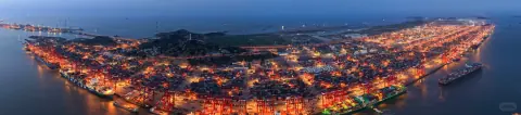 Panoramic view of an illuminated container port surrounded by dark water