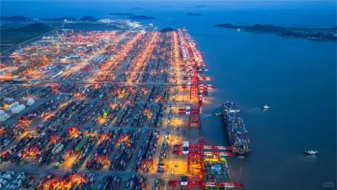 Long illuminated container terminal beside blue sea at dusk