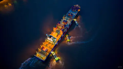 Container ship lit by orange quay lights against dark harbour water