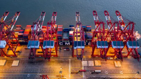 Red quay cranes over a container ship in a brightly lit terminal