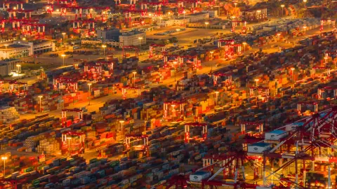 Wide view across container ships and densely lit terminal stacks at night
