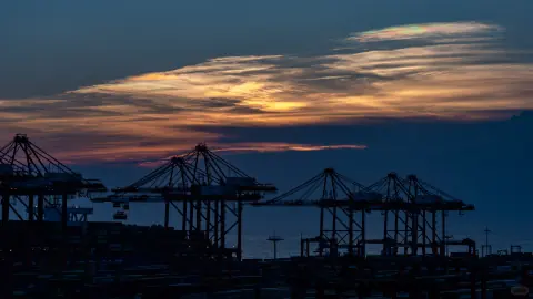 Silhouetted harbour cranes beneath a streaked sunset sky