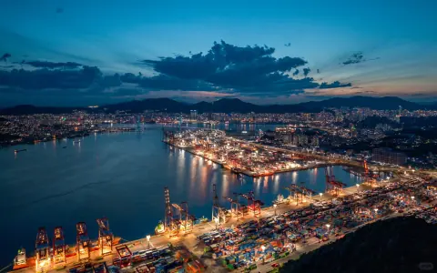 Illuminated container quay beside harbour water and distant mountains