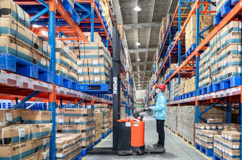 Warehouse operator and pallet truck between tall storage racks