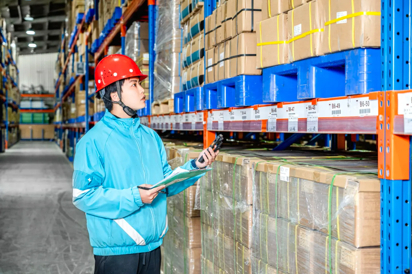 Warehouse worker recording stock beside boxed goods on pallet racks