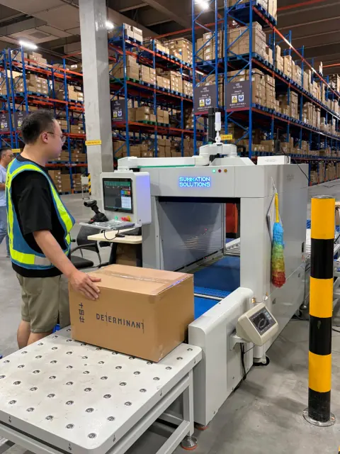 Worker feeding a carton into a warehouse processing station