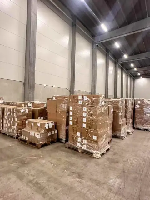 Palletised cardboard cartons stored in a lit warehouse aisle