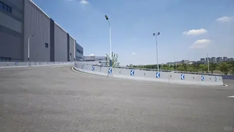 Broad warehouse access road with grey industrial facades and blue sky