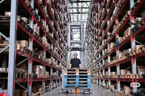 Forklift operator in a long aisle between red warehouse racks
