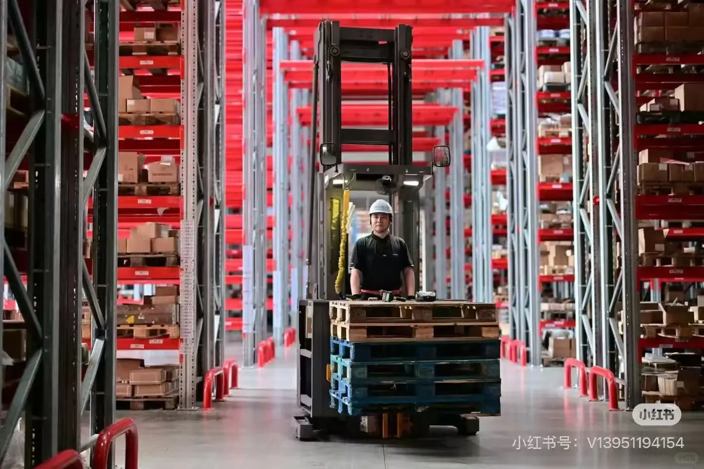 Forklift working between tall red warehouse pallet racks