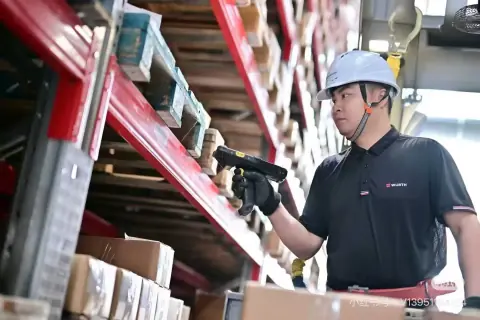 Warehouse operator checking stock beside red pallet racks