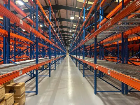Symmetrical view down an empty blue and orange warehouse rack aisle